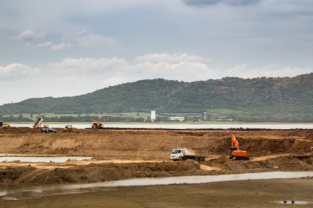 Pelle Rétrocaveuse (excavatrice) Et Camions Dans Le Secteur De La Construction Avec Rivière Et Ciel