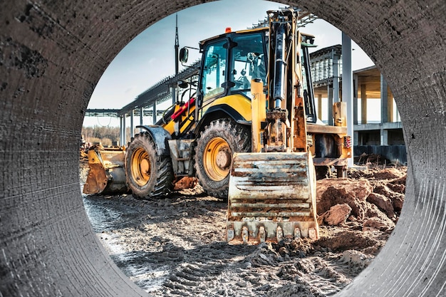 Une pelle universelle travaille sur un chantier de construction contre un ciel nuageux Travaux de terrassement sur un chantier de construction Équipement de terrassement moderne L'entrepreneur effectue des travaux de construction