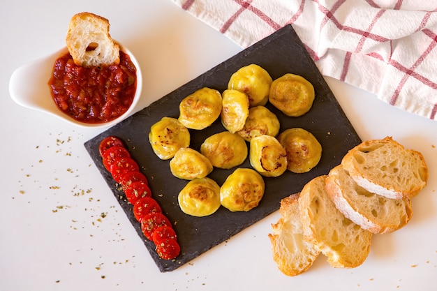 Pelmeni de nourriture russe, boulettes de viande frites sur plaque de pierre, avec tomates, pain et sauce rouge. Vue de dessus, pose à plat.