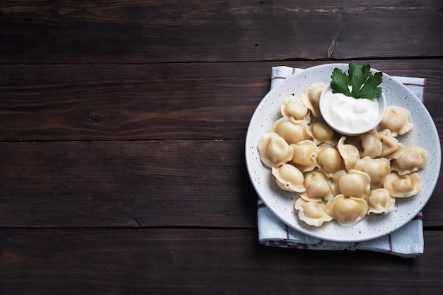 Pelmeni traditionnel, raviolis, boulettes remplies de viande sur assiette, cuisine russe. Fond rustique en bois, copiez l'espace.