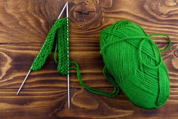 Pelote de laine et aiguilles à tricoter avec tricot sur table en bois. Vue de dessus