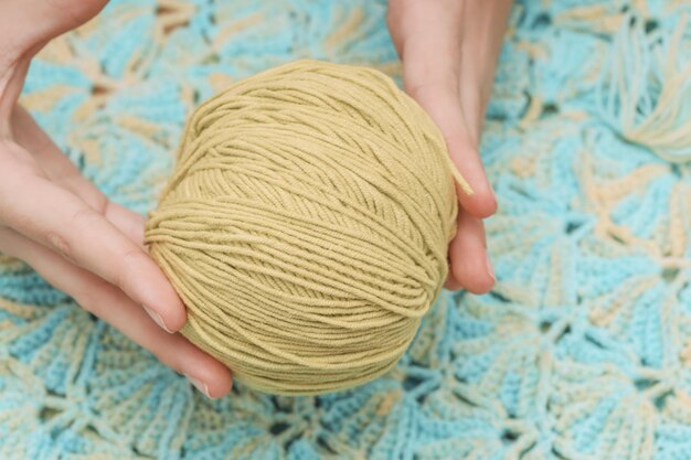 Pelote de laine jaune dans les mains sur le fond d'une nappe tricotée verte Photo de haute qualité