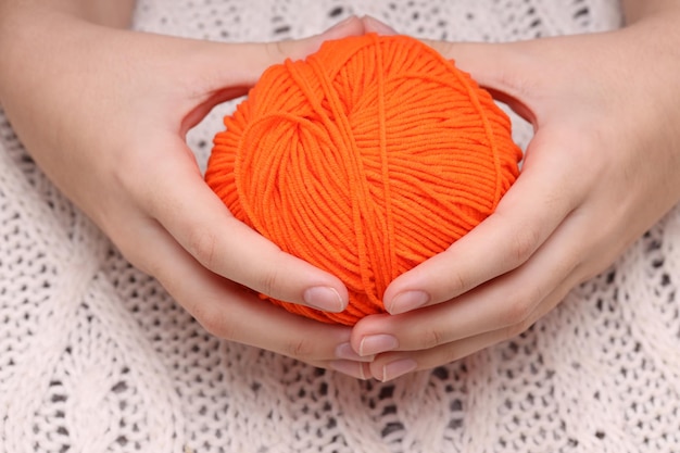 Pelote de laine orange dans les mains sur le fond d'une nappe tricotée blanche. photo de haute qualité