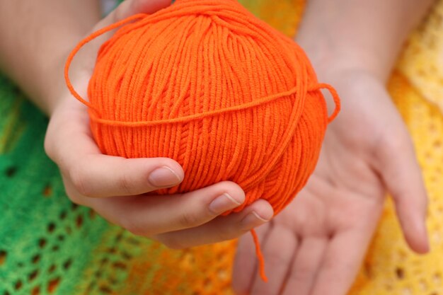 Pelote de laine orange dans les mains sur fond de nappe tricotée vert-jaune. photo de haute qualité
