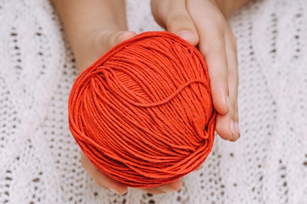 Pelote de laine rouge dans les mains sur le fond d'une nappe tricotée blanche. photo de haute qualité