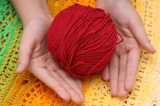 Pelote de laine rouge dans les mains sur fond de nappe tricotée vert-jaune. photo de haute qualité
