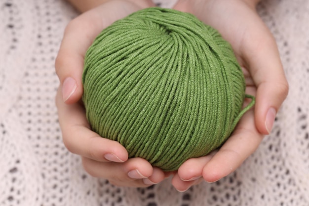 Pelote de laine verte dans les mains sur fond de nappe tricotée blanche. photo de haute qualité