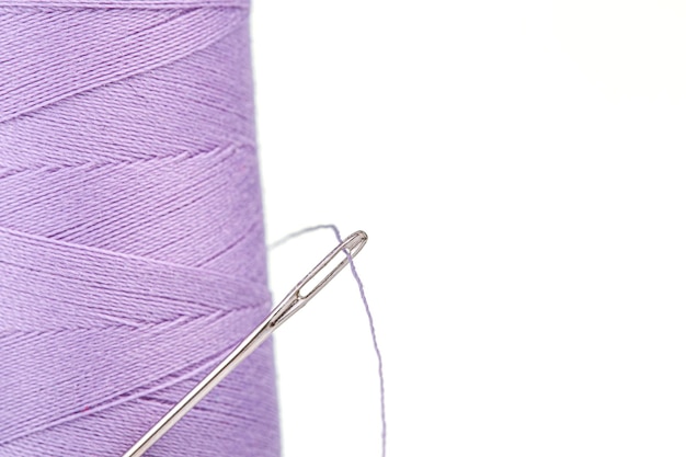Pelote de macro de couleurs violettes de fil avec une aiguille sur un fond blanc