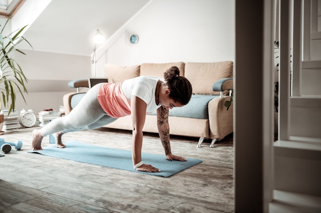 Pendant l'entraînement actif. Jeune femme concentrée faisant des pompes pendant la formation au premier étage de la maison