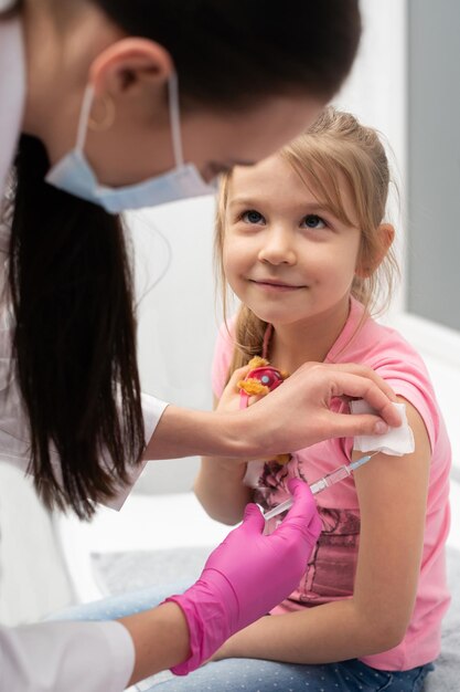 Photo pendant qu'elle reçoit le vaccin, la fille sourit doucement et regarde avec confiance dans les yeux de l'infirmière. le médecin poignarde l'enfant dans le bras avec une aiguille. vaccin préventif pour les jeunes enfants.