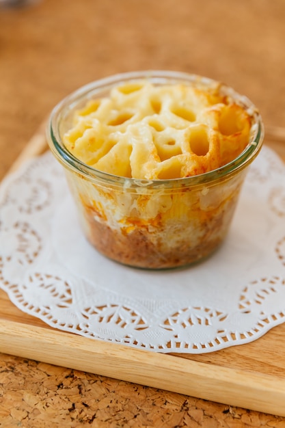 Penne au fromage dans un bol en verre sur une plaque en bois.