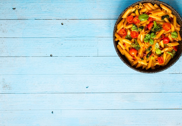 Penne italienne à la sauce tomate et différents types de légumes, sur une table en bois