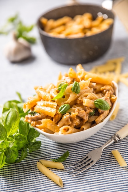 Penne de pâtes aux morceaux de poulet champignons basilic et parmesan Cuisine italienne dans un bol blanc sur la table de la cuisine.