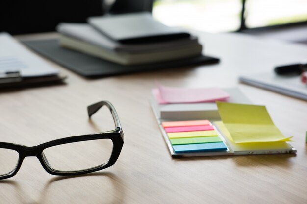 Pense-bête, lunettes, cahier sur le bureau.