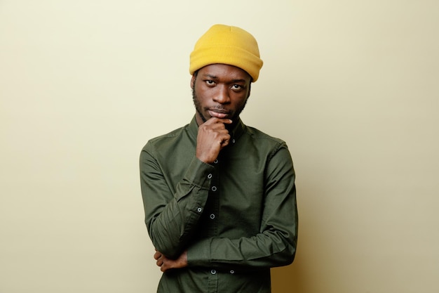 La pensée attrapa le menton jeune homme afro-américain au chapeau portant une chemise verte isolée sur fond blanc