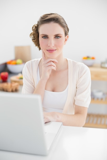 Pensée jolie femme assise dans la cuisine en utilisant son carnet