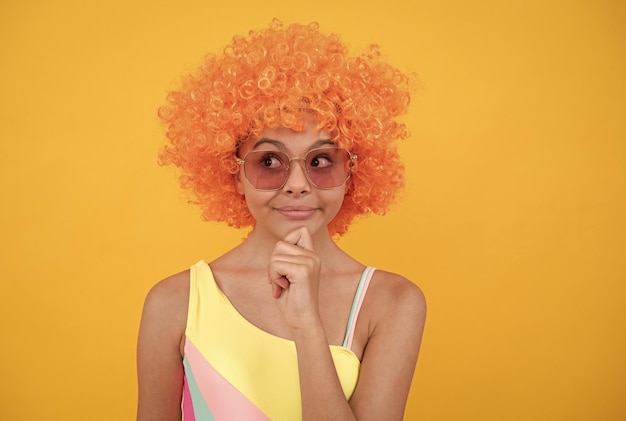 Pensée joyeuse adolescente en lunettes de soleil et maillot de bain portant des cheveux de perruque frisée orange sur fond jaune émotions