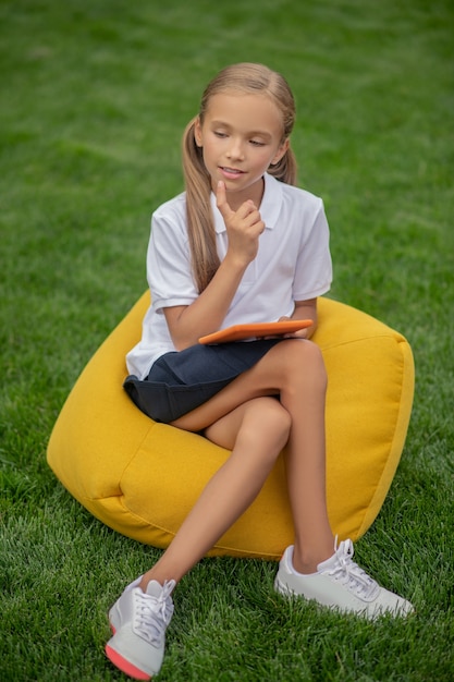 En pensées. Jolie écolière blonde assise sur une chaise de sac et à la réflexion