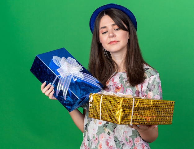 Penser la belle jeune fille portant un chapeau de fête tenant et regardant des coffrets cadeaux