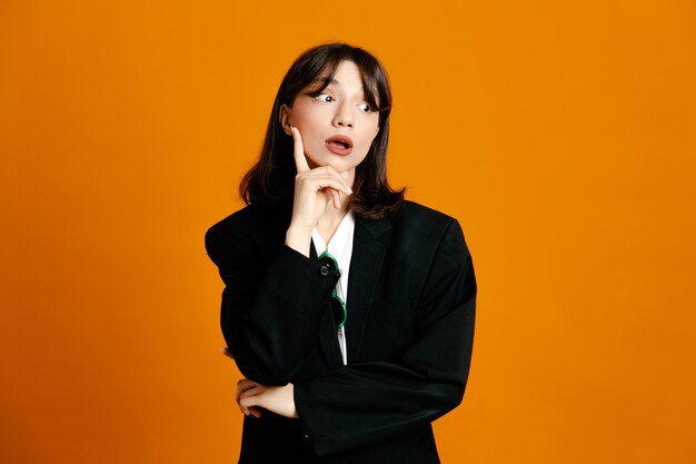 Penser jeune belle femme portant une veste noire isolée sur fond orange