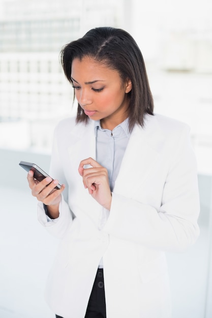 Penser la jeune femme d&#39;affaires aux cheveux sombre en regardant son téléphone portable