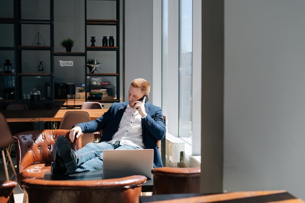 Penser que le jeune homme d'affaires portant un costume de mode parle sur un téléphone portable dans une salle de bureau moderne