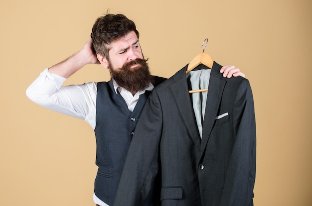 Penser à quoi porter pour un événement formel Hipster choisissant une veste de costume formelle dans une armoire Homme barbu à la boutique de vêtements de cérémonie