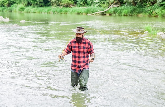 Pensez à Hobby pêcheur barbu dans l'eau homme mûr pêche à la mouche homme attrapant du poisson pêcheur montrer la technique de pêche utiliser la canne week-end d'été pêche à la mouche réussie passe-temps et activité sportive