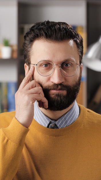 Pensez juste à l'émotion gestuelle. La vue verticale d'un enseignant ou d'un homme d'affaires barbu positif avec des lunettes regardant la caméra et tapotant son doigt sur sa tempe, suggère de bien réfléchir. Coup moyen