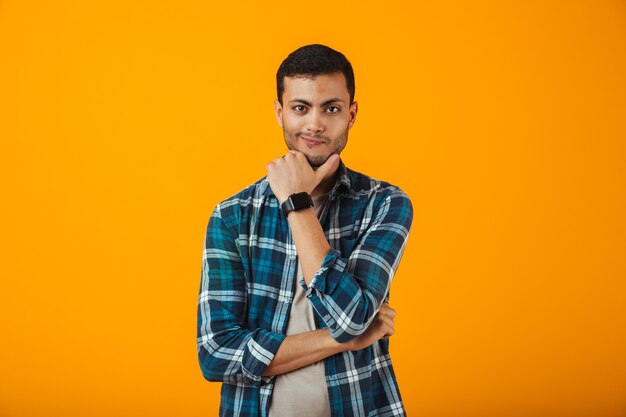 Pensive jeune homme portant une chemise à carreaux debout isolé sur mur orange