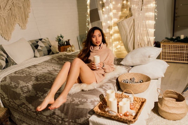 Pensive jeune jolie femme asiatique avec des bougies allumées la veille de Noël faisant des voeux