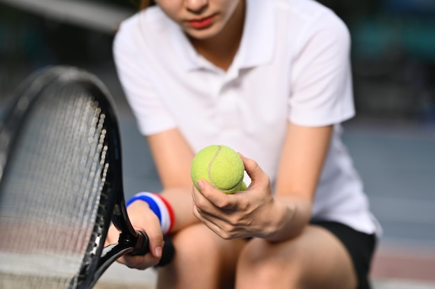 Pensive young female tennis player holding ball racket assis sur le banc au court de tennis