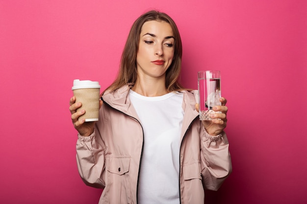 Pensive young woman holding tasse en papier et tasse en verre avec de l'eau