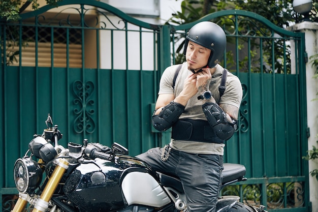 Pensiver homme assis sur une moto, portant des vêtements d'équitation et un t-shirt, fixant son casque