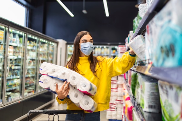 Pénurie de papier toilette Femme avec un masque hygiénique faisant des achats de papier toilette en raison de la panique et de la thésaurisation des produits lors d'une épidémie virale.