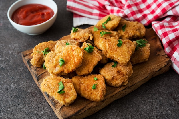 Pépites de poulet maison aux herbes et ketchup sur une planche de bois