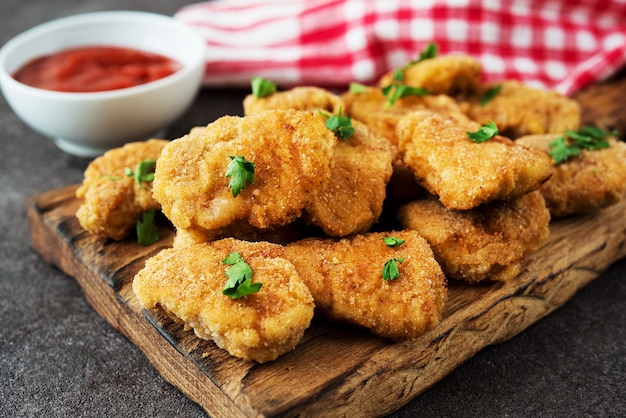 Pépites de poulet maison aux herbes et ketchup sur une planche de bois