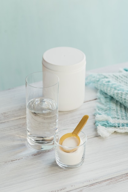 Peptides de collagène hydrolysés de source marine dans un bol en verre et eau sur bois blanc.