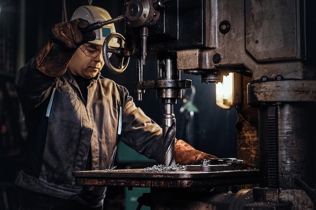 Percer un trou dans le métal avec une perceuse géante à l'usine sidérurgique par un travailleur masculin.