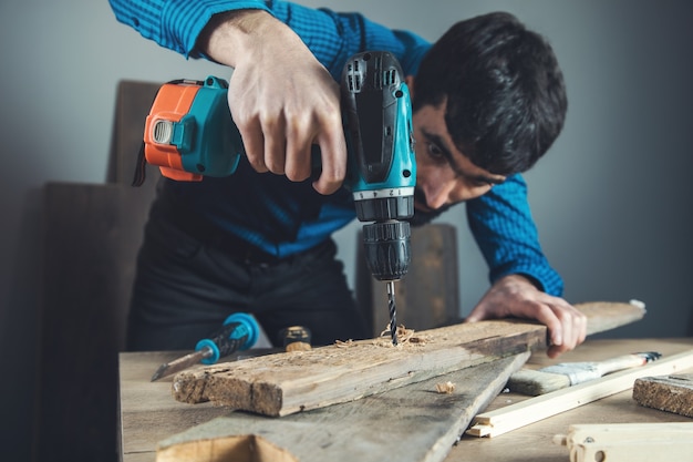 Perceuse électrique de main d'homme de travailleur avec du bois