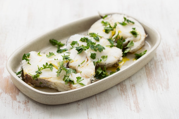 Perche bouillie avec du persil et de l'huile d'olive sur un plat sur une surface en bois blanc