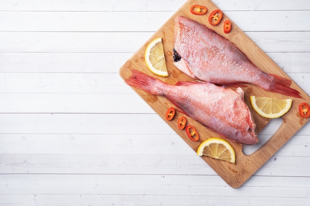 Perche de poisson cru sans tête avec des tranches de citron et des piments rouges sur une planche à découper en bois