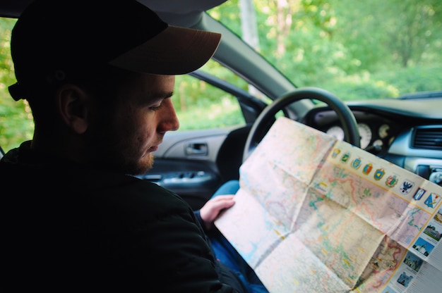 Perdu dans la forêt jeune conducteur assis dans la voiture tout en tenant la carte et en regardant de côté