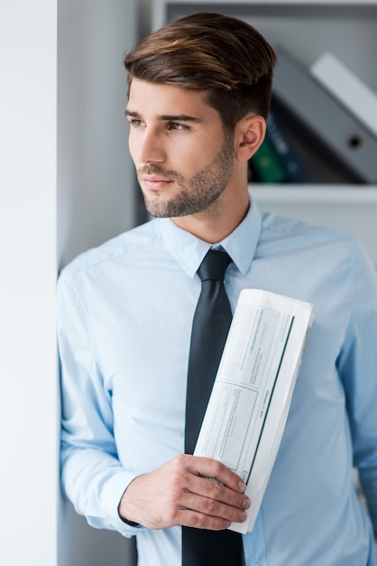 Perdu dans des pensées d'affaires. Gentil jeune homme en chemise et cravate tenant le journal