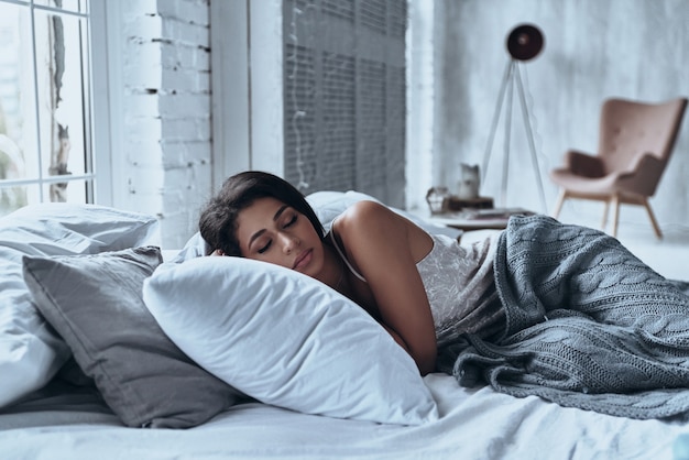 Perdu dans un sommeil profond. Jolie jeune femme gardant les yeux fermés en position allongée sur le lit à la maison