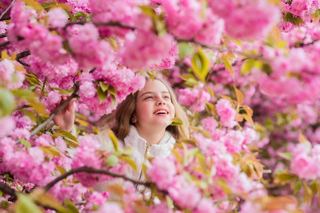 Perdu en fleur. Notion de botanique. Fille appréciant le sakura de fleur de cerisier. Un enfant mignon profite d'une chaude journée de printemps. Floraison tendre. Touriste de fille posant près de sakura. Enfant sur les fleurs roses du fond d'arbre de sakura.