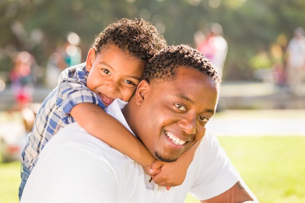 Un père afro-américain heureux et son fils mixte jouent dans le parc.