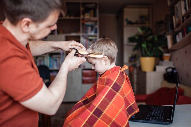 Père d'âge moyen coupant les cheveux de son petit fils seul à la maison