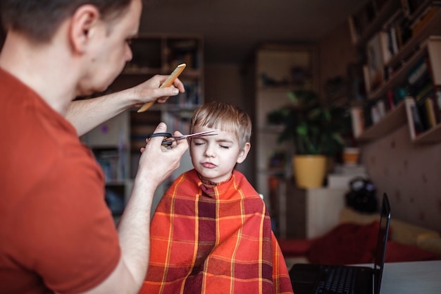 Photo père d'âge moyen coupant les cheveux de son petit fils seul à la maison