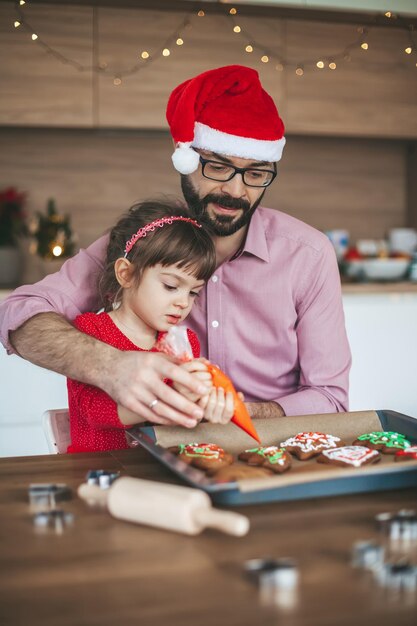 Père aidant sa fille à décorer des biscuits de Noël